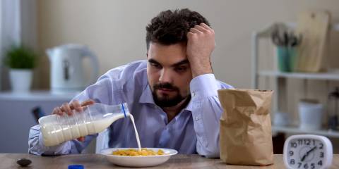 a very tired man pouring milk on his breakfast cereal