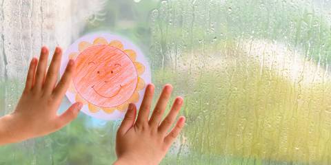 a child holding a paper sun up to a window on a rainy day