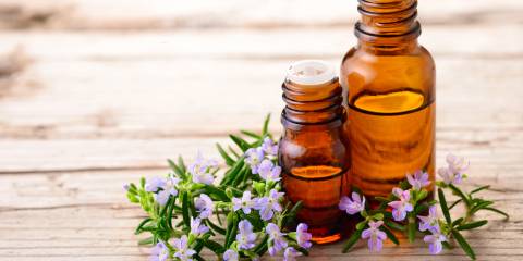 Blooming rosemary sprigs on a wooden table with essential oils in brown bottles.
