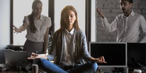 a woman meditating in an office with stressful coworkers