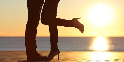 Silhouette of a couple's legs while embracing on the beach with the sun in the background at sunset.