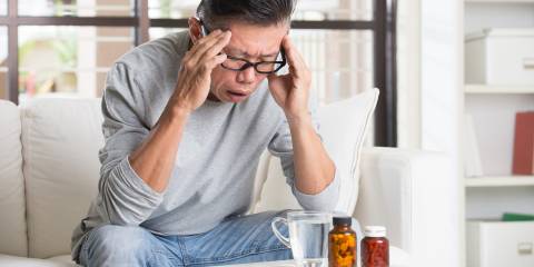 a middle-aged man with a headache leaning over tea and supplements