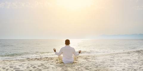 A man meditating on the beach facing a calm sea