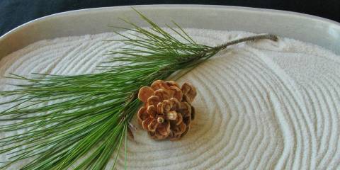 A personal zen garden with a sprig of pine and a pine cone on it.