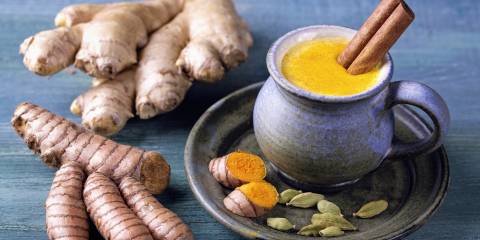 A mug of Golden Milk with turmeric and ginger root beside it.