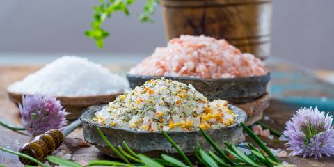 Different types of natural salt in stone bowls on wooden surface.