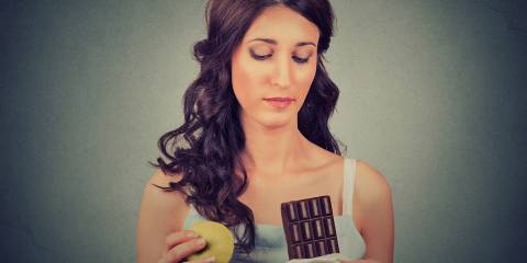 Woman with chocolate and apple trying to make a healthy choice.