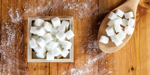 Sugar cubes in a box next to a wooden spoon filled with sugar cubes.