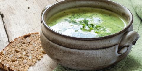 Pottery bowl filled with green broccoli soup with parsley garnish. 