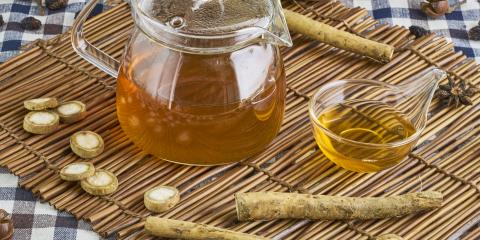 Small glass teapot of golden tea surrounded by burdock roots on a bamboo mat.