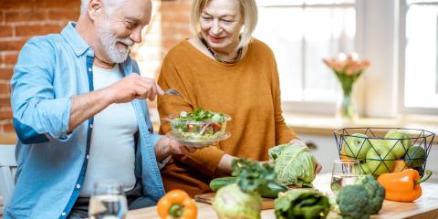 A senior man eating from a salad while a senior woman looks on.