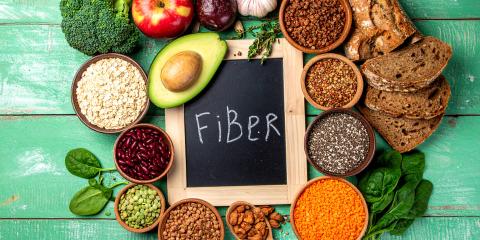 The word fiber on a blackboard slate surrounded by food sources of fiber, like avocado, beans, and lentils.