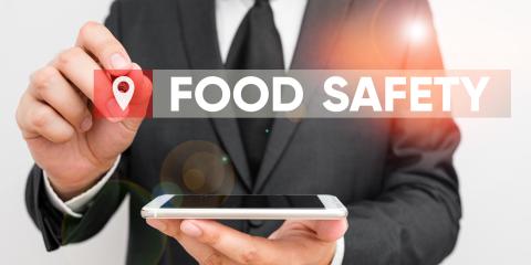 Man in suit holds cell phone flat in one hand and with other is pointing to the words Food Safety