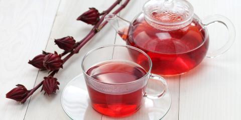 Hibiscus tea in a glass cup in front of a glass tea kettle. 