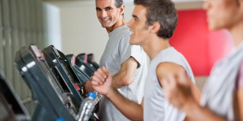 Middle aged man on a treadmill smiling at a younger male on another treadmill