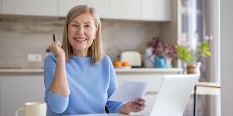 Middle-aged woman working happily in front of a computer in her kitchen.