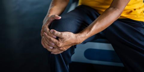Senior Asian man in work-out gear holding an aching knee.