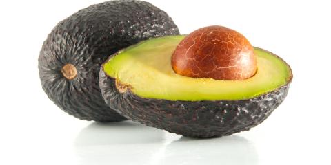 A green avocado cut in half with a pit showing.