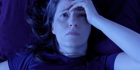 A worried-looking woman lying in bed at night, holding her head in her left hand. 