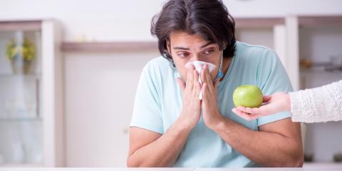 Young man looking at fruit and sneezing into a tissue.