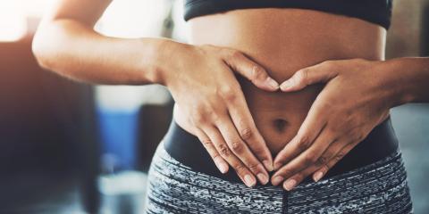 Woman with sports bra, using hands to create a heart over navel.