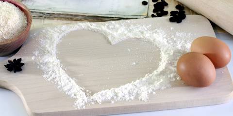 cooking utensils, eggs, and flour on a cutting board in a heart design