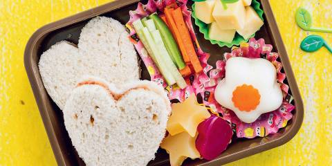 a bento box with heart-shaped sandwiches, homemade fruit snacks, cubed cheese, and veggie sticks.