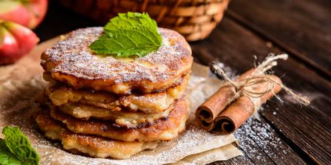 Apple Jack Pancakes stacked on a piece of parchment paper sprinkled with powdered sugar.