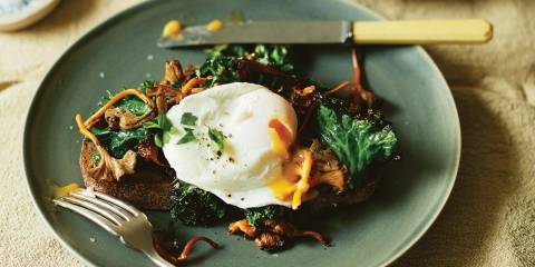 Chanterelle Toast with Poached Eggs and Kale on a plate with yolk pouring out of the egg.