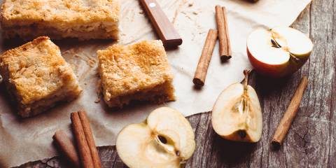 Apple cake with halved apples and cinnamon sticks on a rustic wooden table.