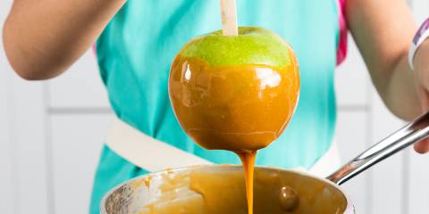 A woman dipping a Granny Smith apple in a pot of caramel to make caramel apples.