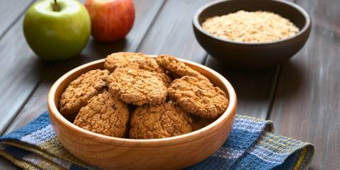 Apple Pie Cookies in wooden bowl with apples and oatmeal in the background.
