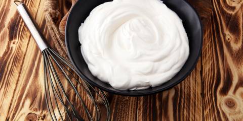 Homemade Whipped Cream in a black bowl with a whisk on a wooden table.
