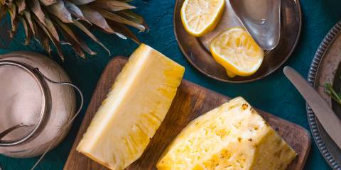 Pineapple on a cutting board with sliced lemons and a jar of sugar on a dark blue background.