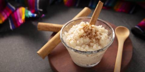 Mexican rice pudding in a glass cup beside a wooden spoon. 