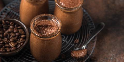 Chocolate mousse in clear glass jars, next to a small dish of coffee beans on a wire metal trivet.