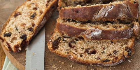 Walnut & Raisin Loaf sliced on a round wooden cutting with bread knife.