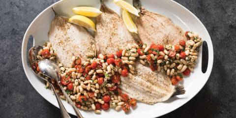 A top view of Roasted Trout with White Bean and Tomato Salad on a white serving tray with a charcoal gray background.