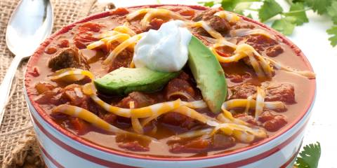 a bowl of chili con carne, topped with cheese, avocado, and sour cream