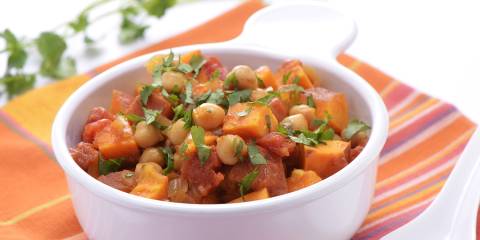 a bowl of curry full of sweet potatoes, chickpeas, and greens
