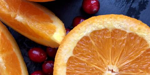 Cranberries and sliced oranges on a dark blue background.