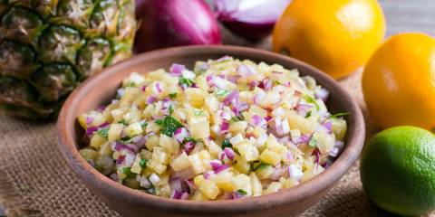 Pineapple mango salsa in a bowl surrounded by the ingredients. 