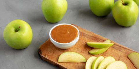 Caramel dip in a bowl on a cutting board with sliced green apples. 