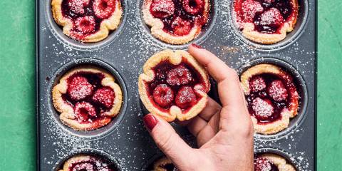 a woman removing raspberry tarts from a cupcake tin