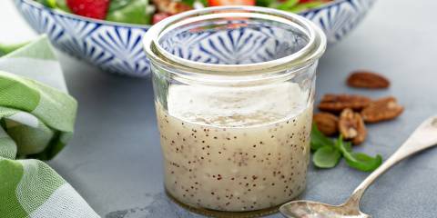 a jar of poppy seed dressing in front of a strawberry salad
