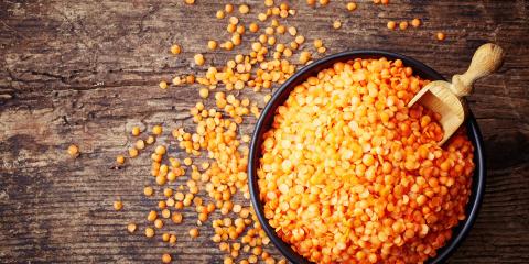 A bowl of uncooked red lentils with a wooden scoop in it. 