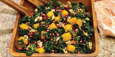Kale, Butternut Squash, & Pomegranate Salad in a wooden salad bowl with wooden salad utensils.