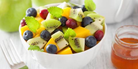 a bowl of kiwi, melon, blueberries, and grapes, with a honey sauce