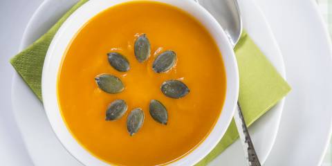Creamy pumpkin soup, in a white bowl, decorated with seeds in a sunburst pattern.