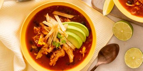 a bowl of spicy red chicken soup with avocado